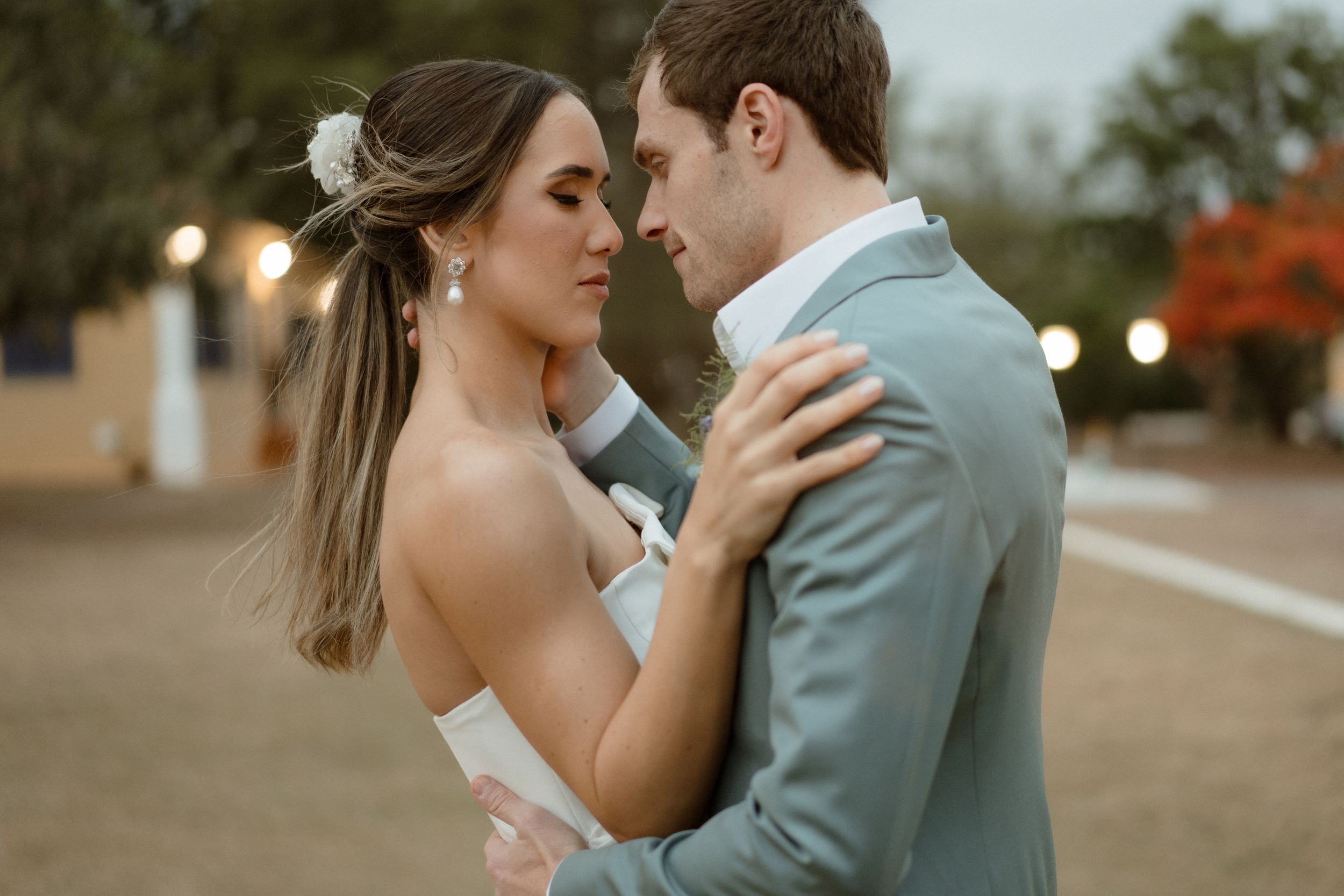 An intimate moment between newlyweds outside at dusk with string lights glowing in the background.