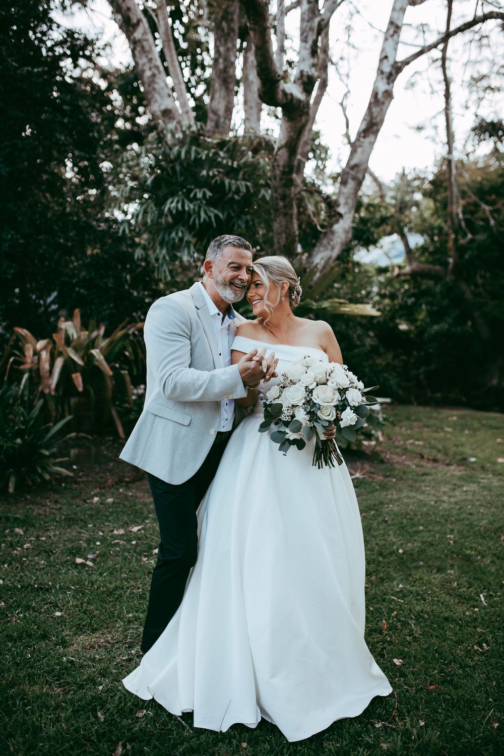 A happy couple shares a candid laugh together in their wedding attire while standing in a garden setting.