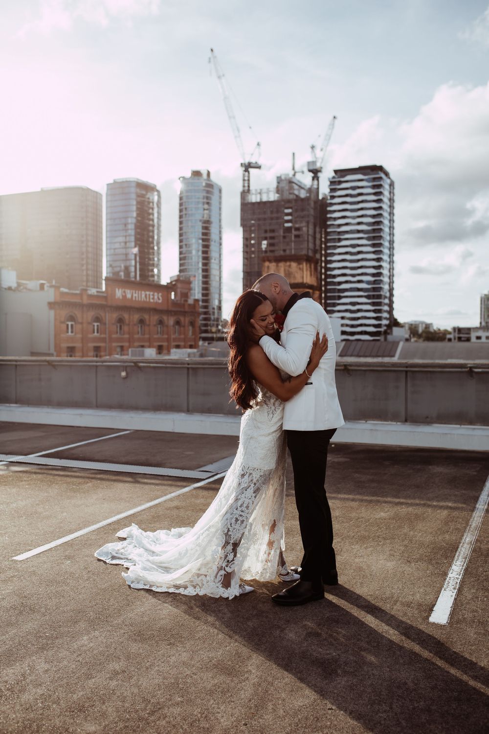 A romantic rooftop moment between a couple in wedding attire with city skyscrapers and construction cranes in the background.
