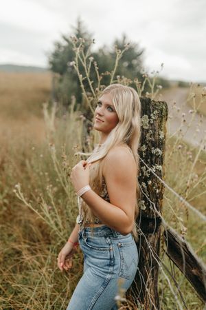 Rustic outdoor portrait by a wooden fence post in a golden field at sunset. Virginia graduation/senior session.