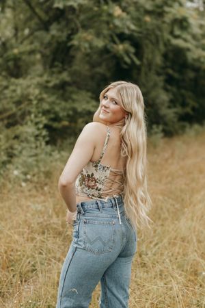 A fashionable summer outfit featuring a floral corset top and high-waisted jeans in a sunny field setting. Virginia graduation/senior sessio