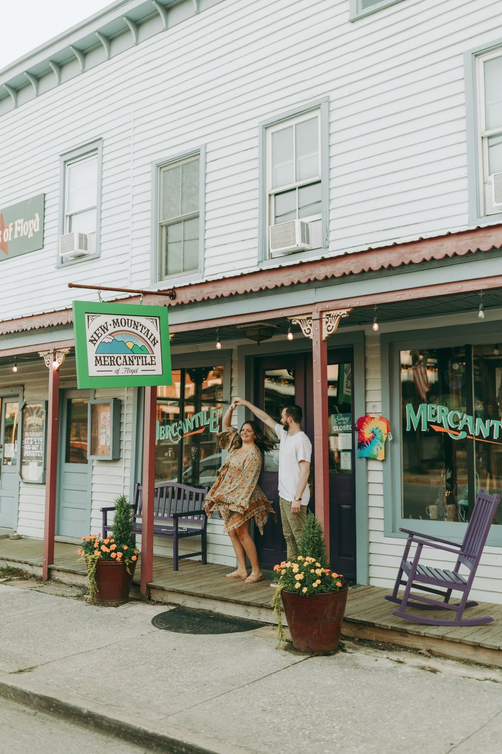 Couple posing playfully outside historic white clapboard building with vintage storefronts. Floyd, VA