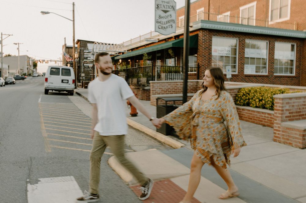 Playful couple holding hands while walking on city sidewalk. Floyd, VA