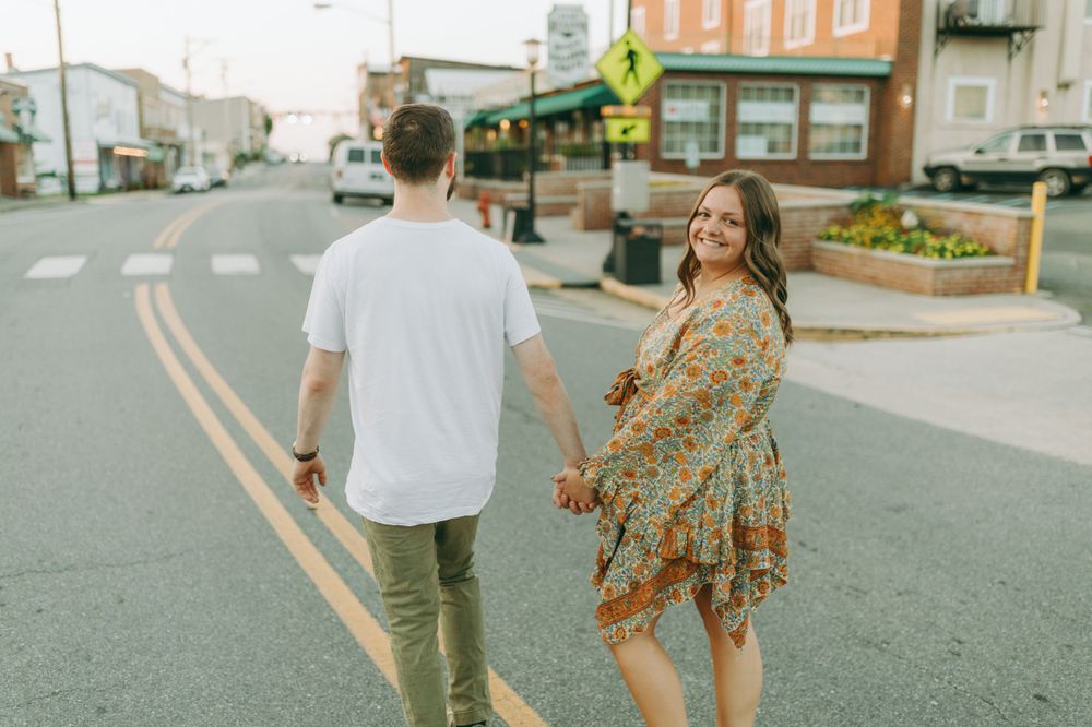 A playful couple strolling down a city street with yellow road lines visible. Floyd, VA