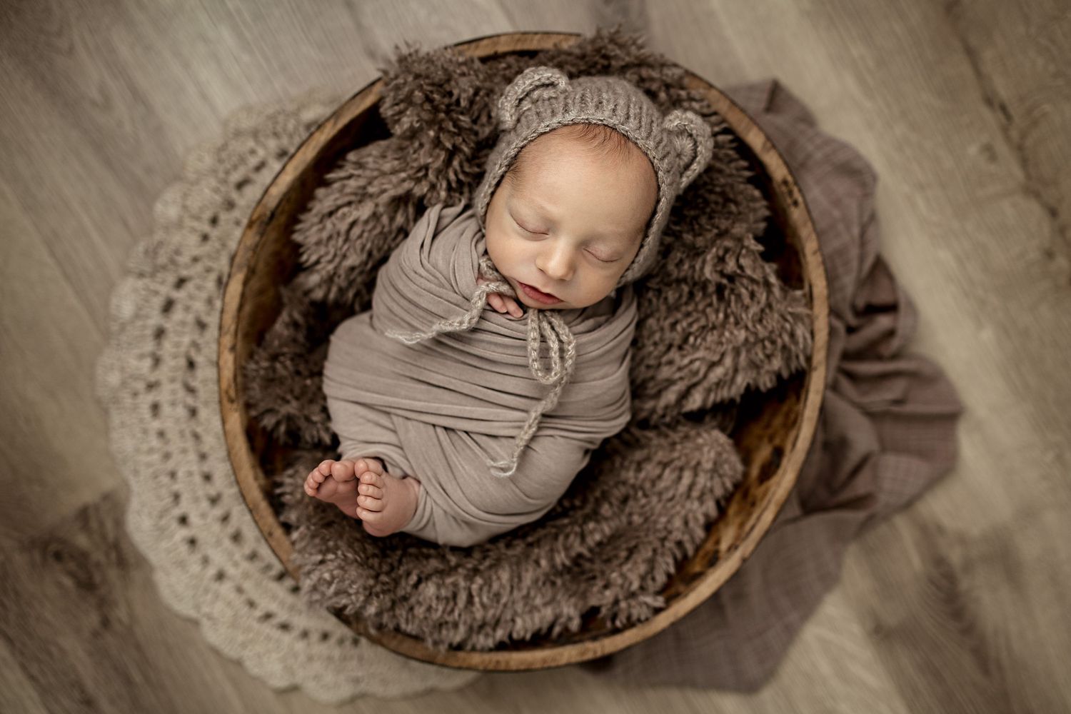 Close-up of sleeping newborn baby wearing soft pink knit sweater against pink textured background.