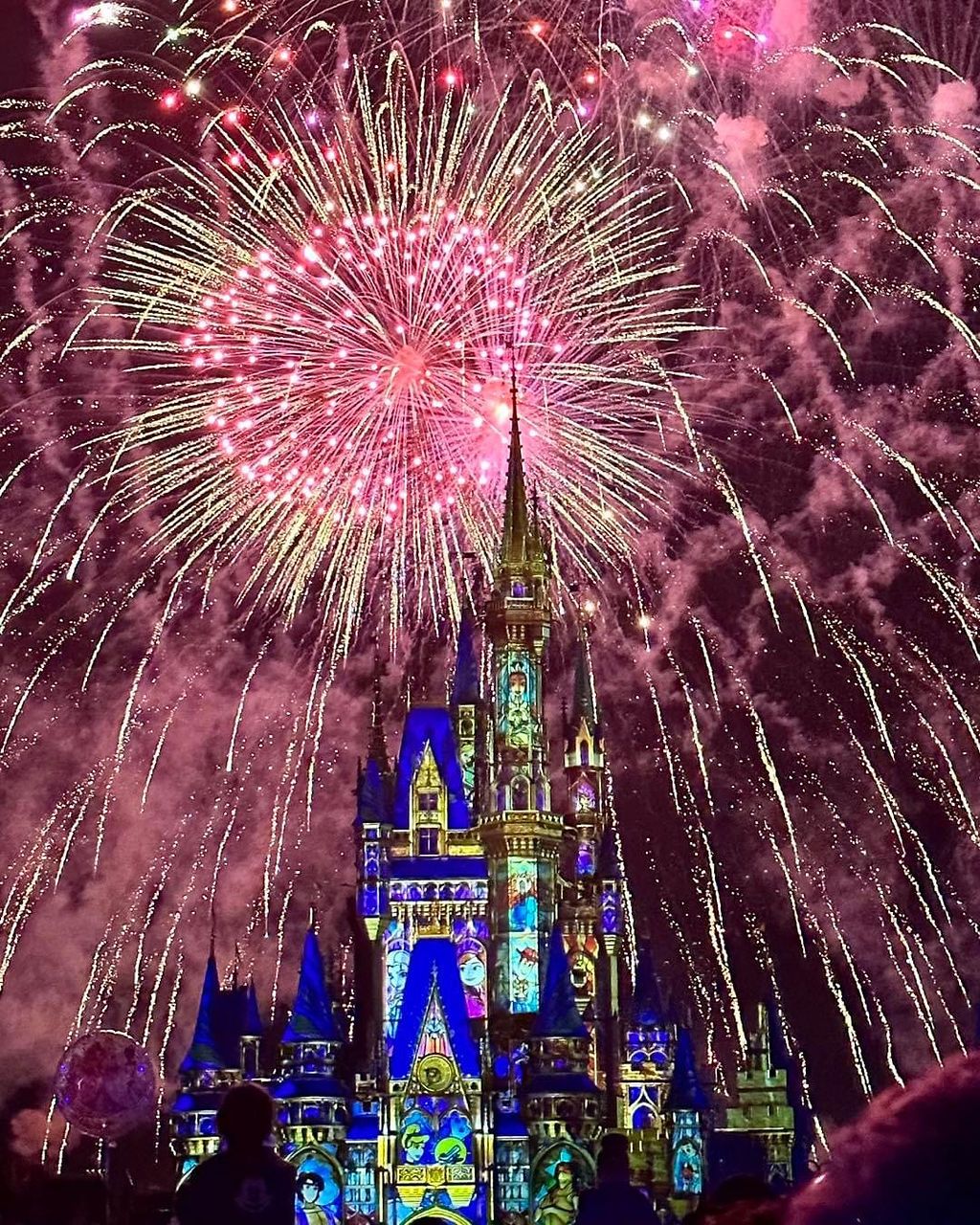 Spectacular pink and white fireworks illuminate Disney's Cinderella Castle lit in blue during a magical nighttime show.