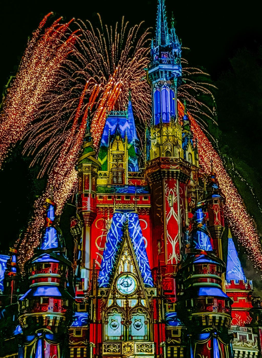 Colorful fireworks burst behind Disney's Cinderella Castle illuminated in vibrant blue, red and yellow lights at night.