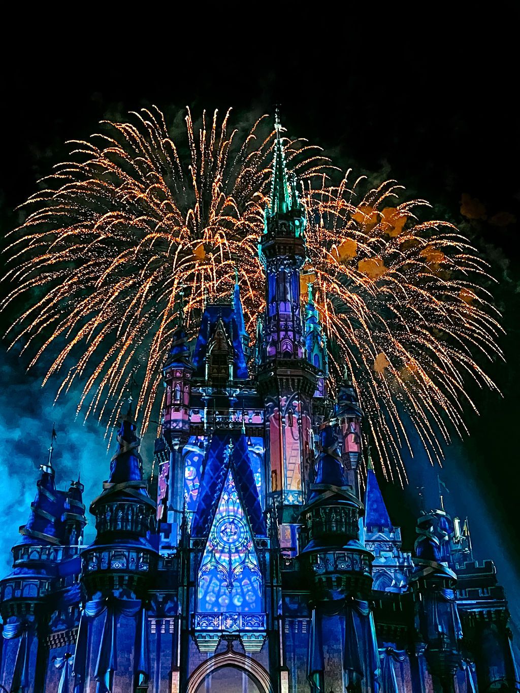 Colorful fireworks explode over Disney World's Magic Kingdom castle illuminated in brilliant blue and purple lights.