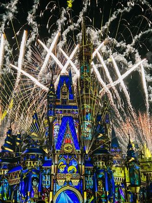 Spectacular fireworks illuminate Cinderella Castle at Disney World with blue lights and white pyrotechnics against dark sky.
