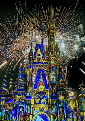 Cinderella Castle at Disney World illuminated in blue and gold with spectacular fireworks bursting in the night sky above.