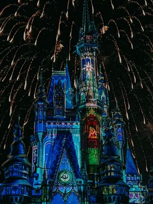 Cinderella Castle at Disney World illuminated in blue with fireworks bursting overhead during a nighttime show.