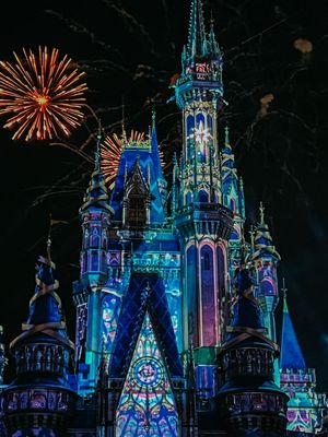 Fireworks burst over Cinderella Castle at Walt Disney World as it glows in vibrant blue and purple nighttime lighting.