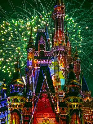 Fireworks burst behind Disney's Cinderella Castle illuminated in vibrant rainbow colors during a nighttime spectacular.