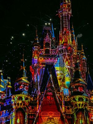 Cinderella Castle at Disney World illuminated with vibrant red, blue and purple lights during a nighttime show.