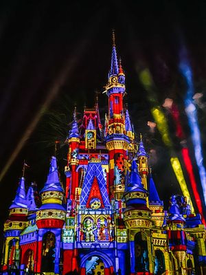 Disney castle lit up at night in vibrant red and blue colors with colorful spotlights illuminating the magical scene.