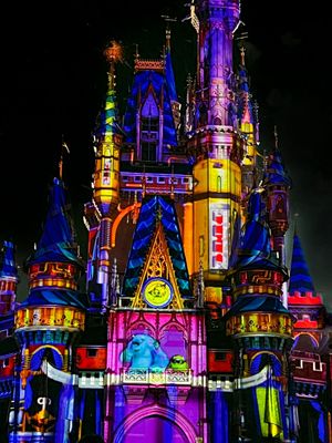 Disney castle illuminated at night with vibrant purple, blue, and yellow lights creating a magical fantasy atmosphere.
