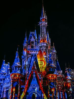 Cinderella Castle at Disney World illuminated at night with vibrant blue and red lighting creating a magical display.