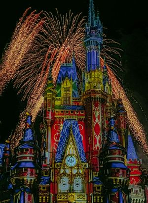 Colorful fireworks burst behind Disney's Cinderella Castle illuminated in vibrant blue, red and gold lights at night.