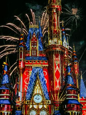 Fireworks bursting behind Cinderella Castle at Disney World with vibrant red and blue nighttime lighting displays.
