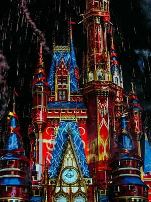 Illuminated Disney castle at night with colorful red and blue lighting effects creating a magical nighttime display.