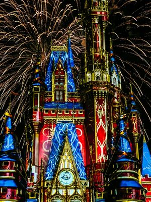 Fireworks burst behind Disney's Magic Kingdom castle illuminated in vibrant blue and red lights during a nighttime show.