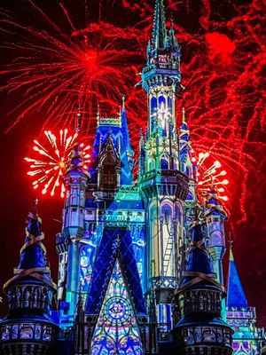 Cinderella Castle at Disney World lit up in blue and white with red fireworks bursting dramatically in the night sky.