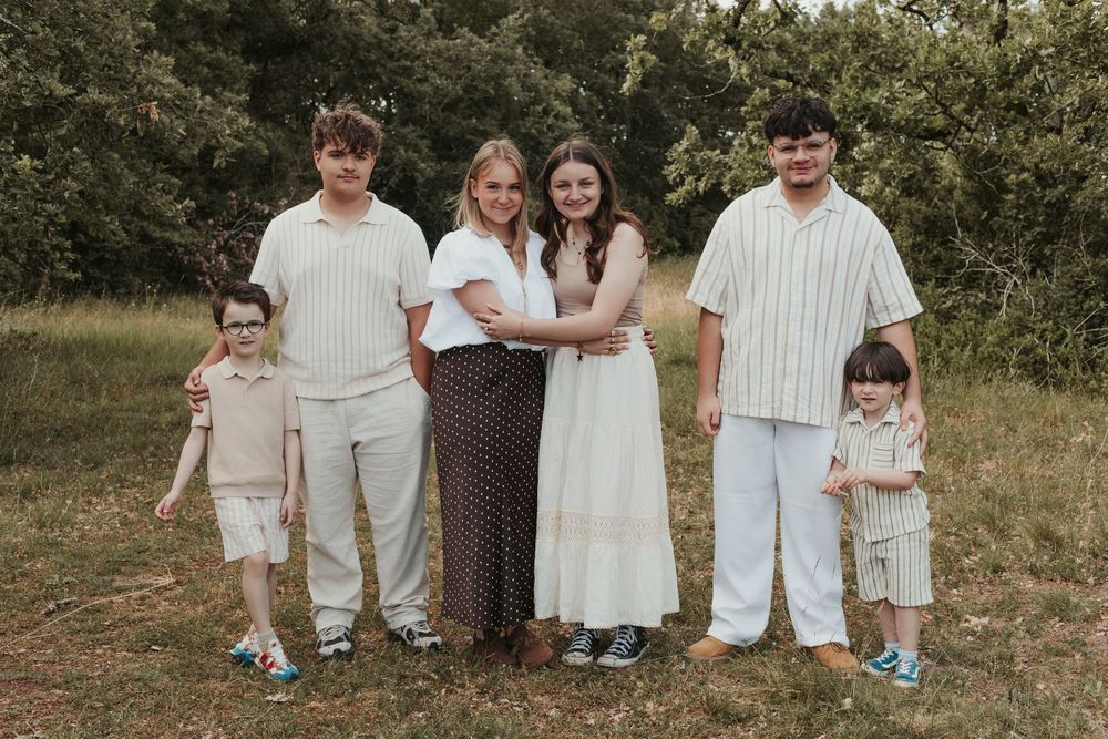 Family of six posing outdoors in a grassy field, wearing coordinated neutral outfits, smiling together.