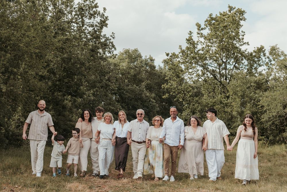 Large multigenerational family posing together outdoors in a green meadow, wearing coordinated neutral beige and white outfits.