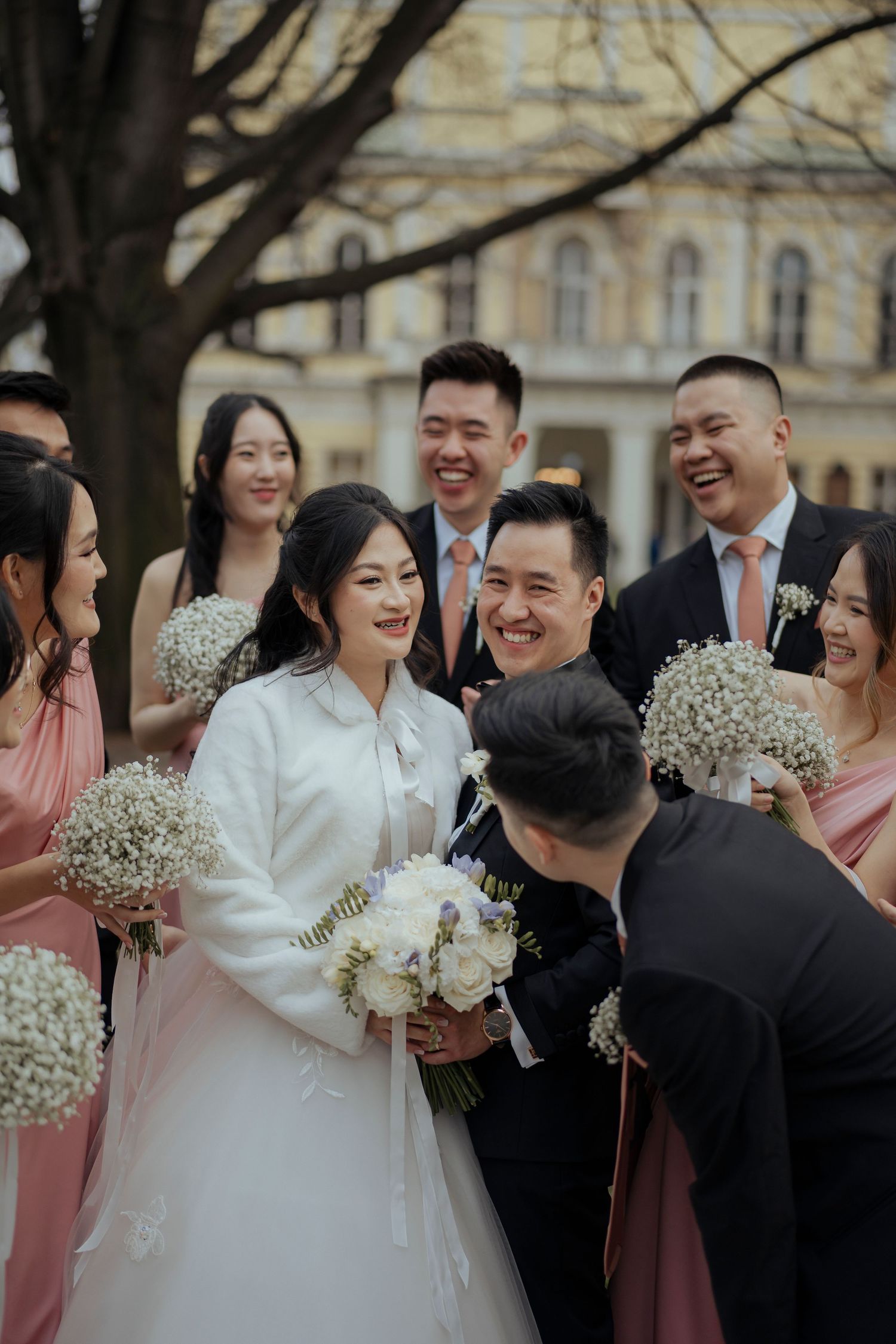 Wedding party in pink bridesmaid dresses and white flowers celebrating outdoors.