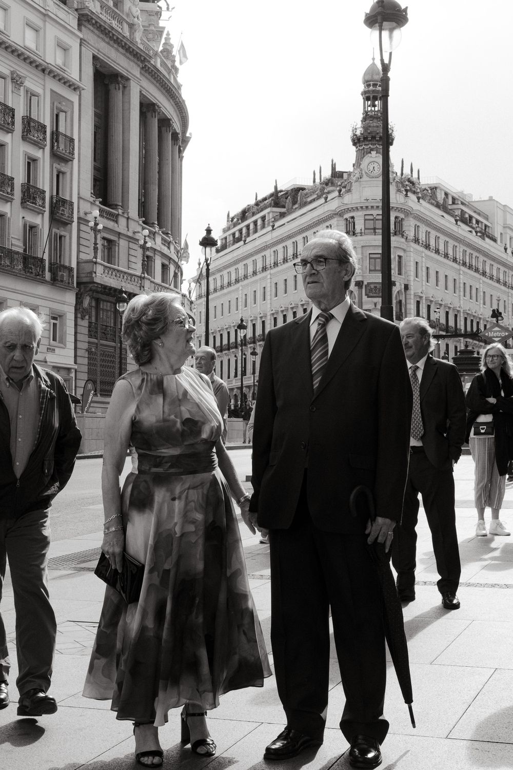 People walking along an elegant European city street with classical architecture in the background.