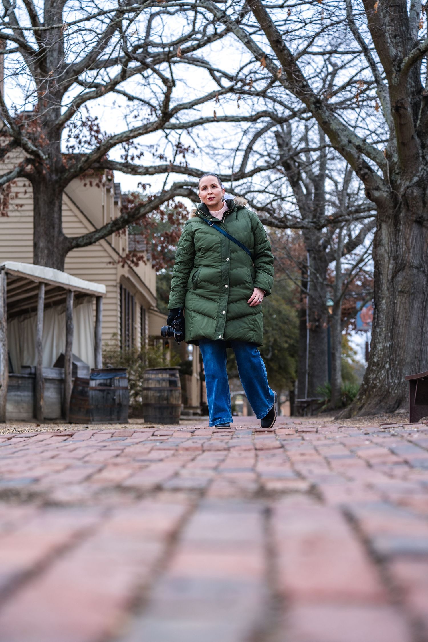 Someone in a green winter coat walks along a brick pathway near a house on a cold winter day.