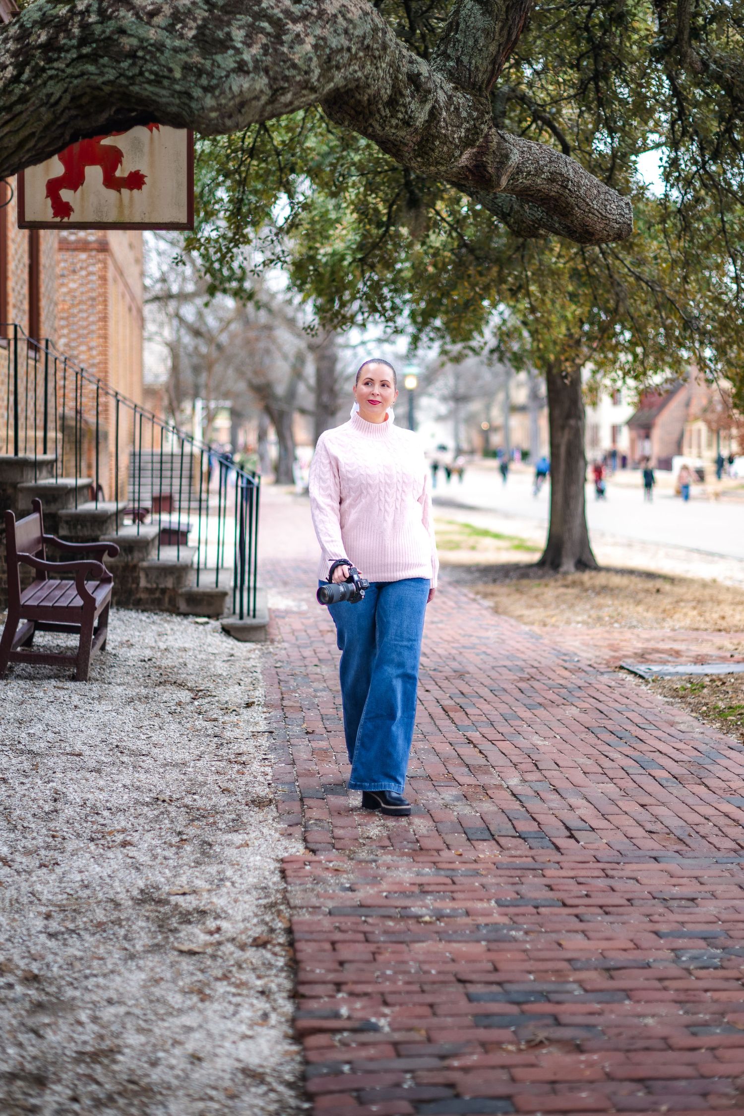 Person walks along historic brick sidewalk in front of brick buildings and beneath large oak tree branches.