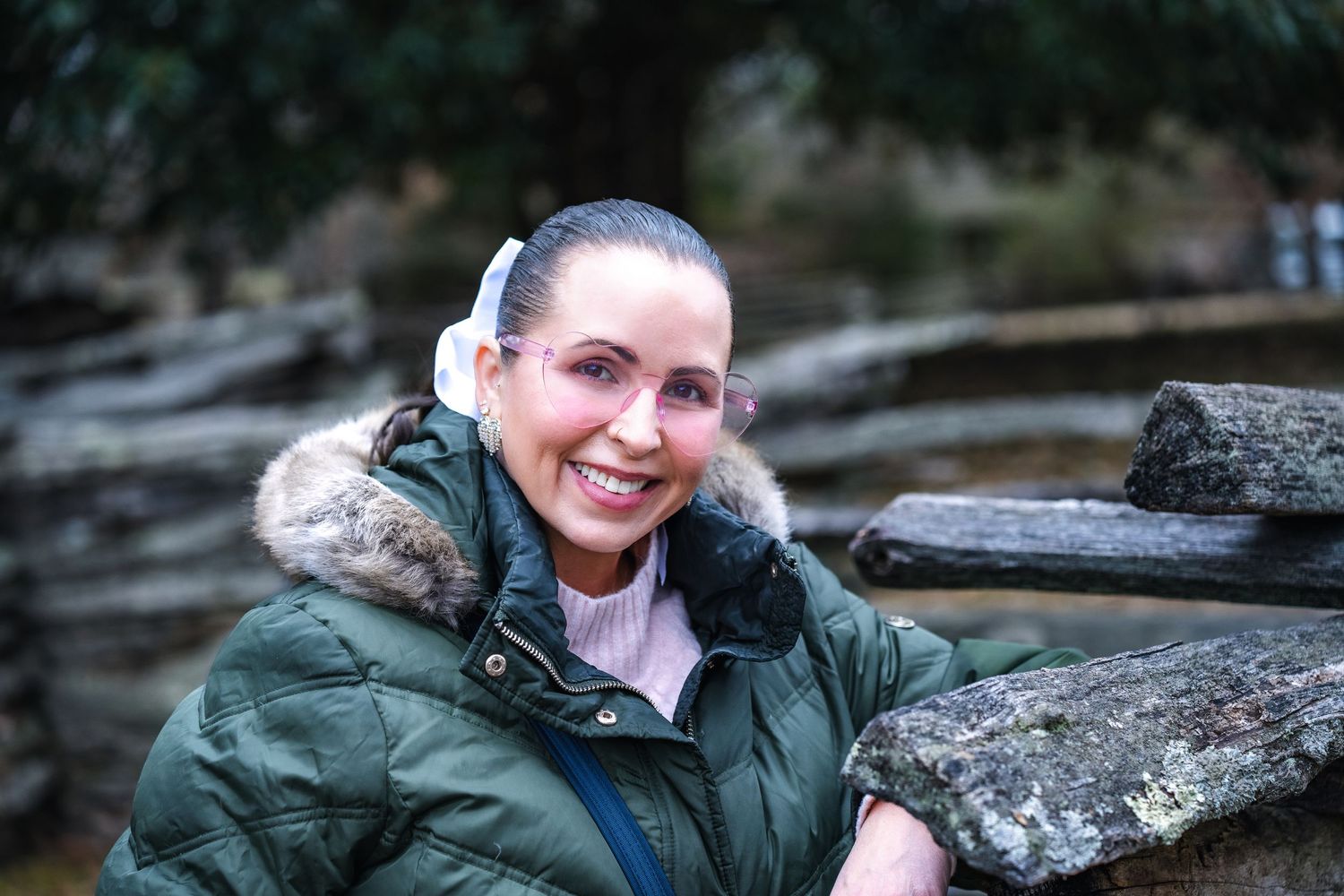 A hiker in a green winter coat with fur-lined hood smiles while resting against rocks in an outdoor setting.