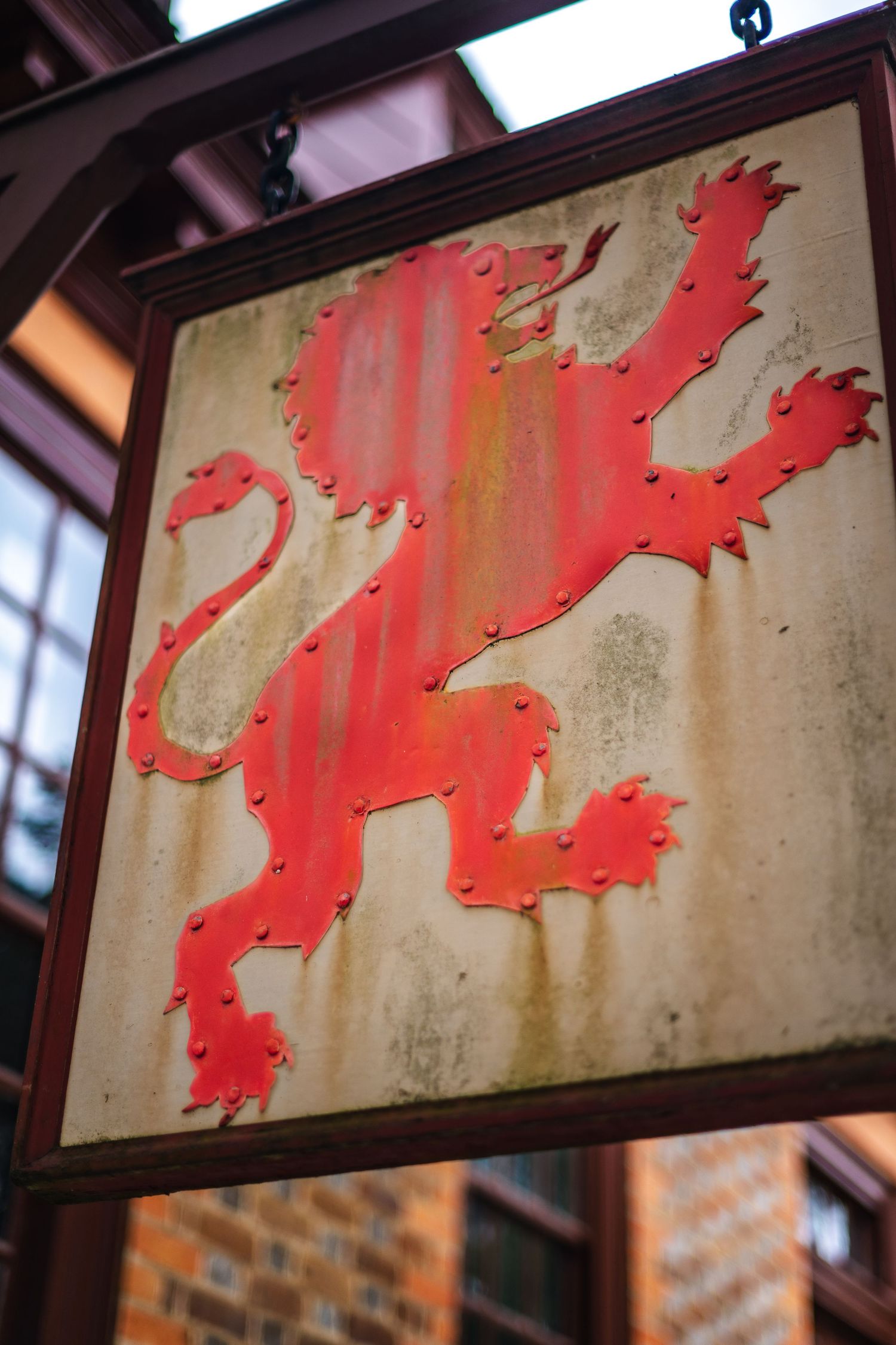 A weathered red heraldic lion rampant symbol painted on a beige metal sign in a wooden frame.