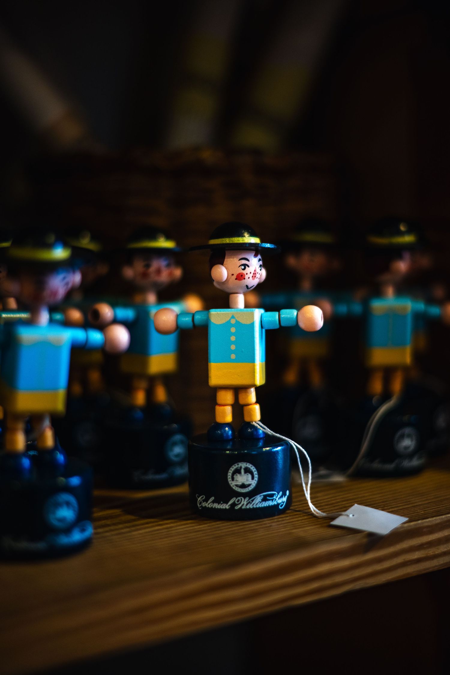 Small wooden toy soldiers with blue and yellow uniforms stand in a row on a dark wooden surface.