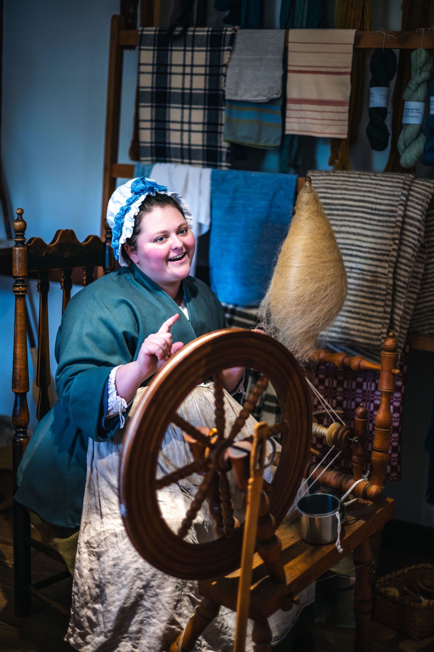Colonial reenactor in period clothing demonstrates traditional spinning on an antique wooden spinning wheel.