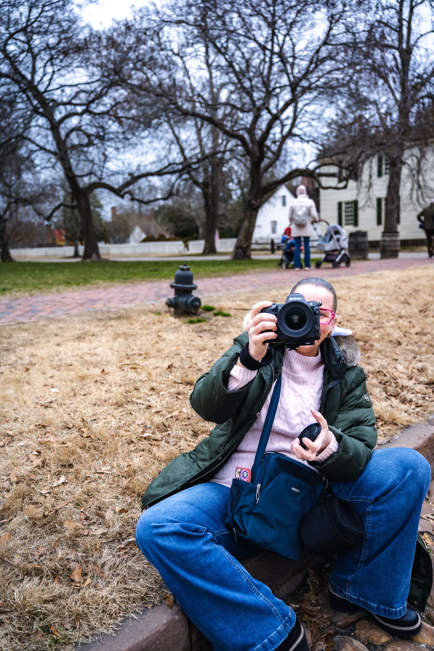 Photographer sitting on the ground with professional camera at historic site with rustic building in background.