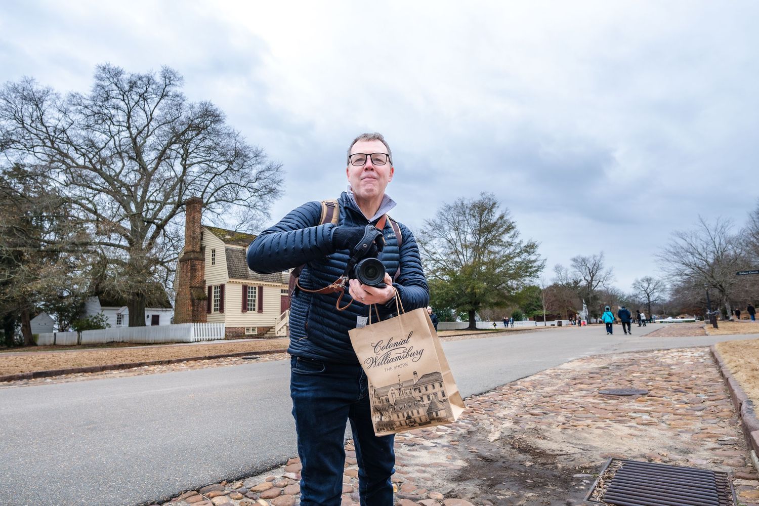 A person holding a handmade cardboard sign stands on a brick walkway with bare winter trees in the background.