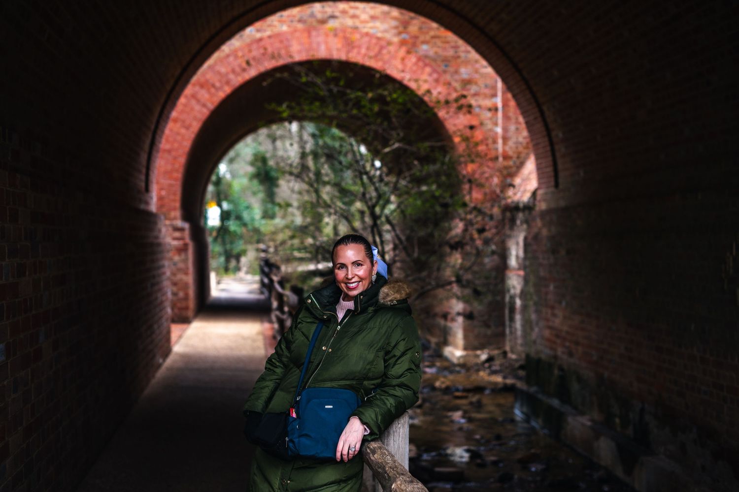 Someone sits in the entrance of a historic stone archway tunnel with moss covered walls.