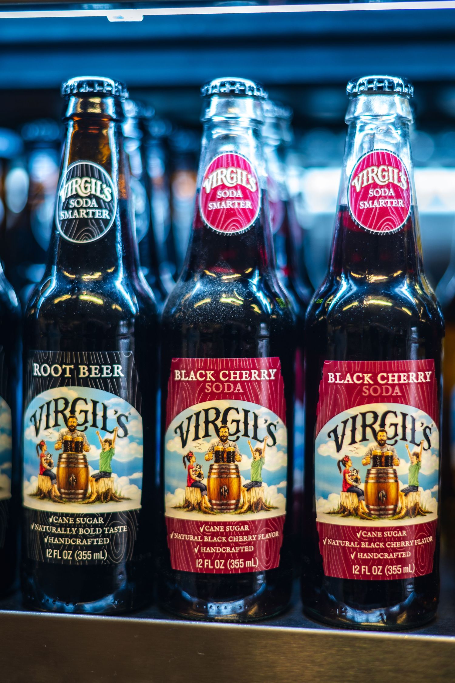 Three glass bottles of Virgil's craft sodas showing root beer and black cherry flavors with vintage-style labels on display.
