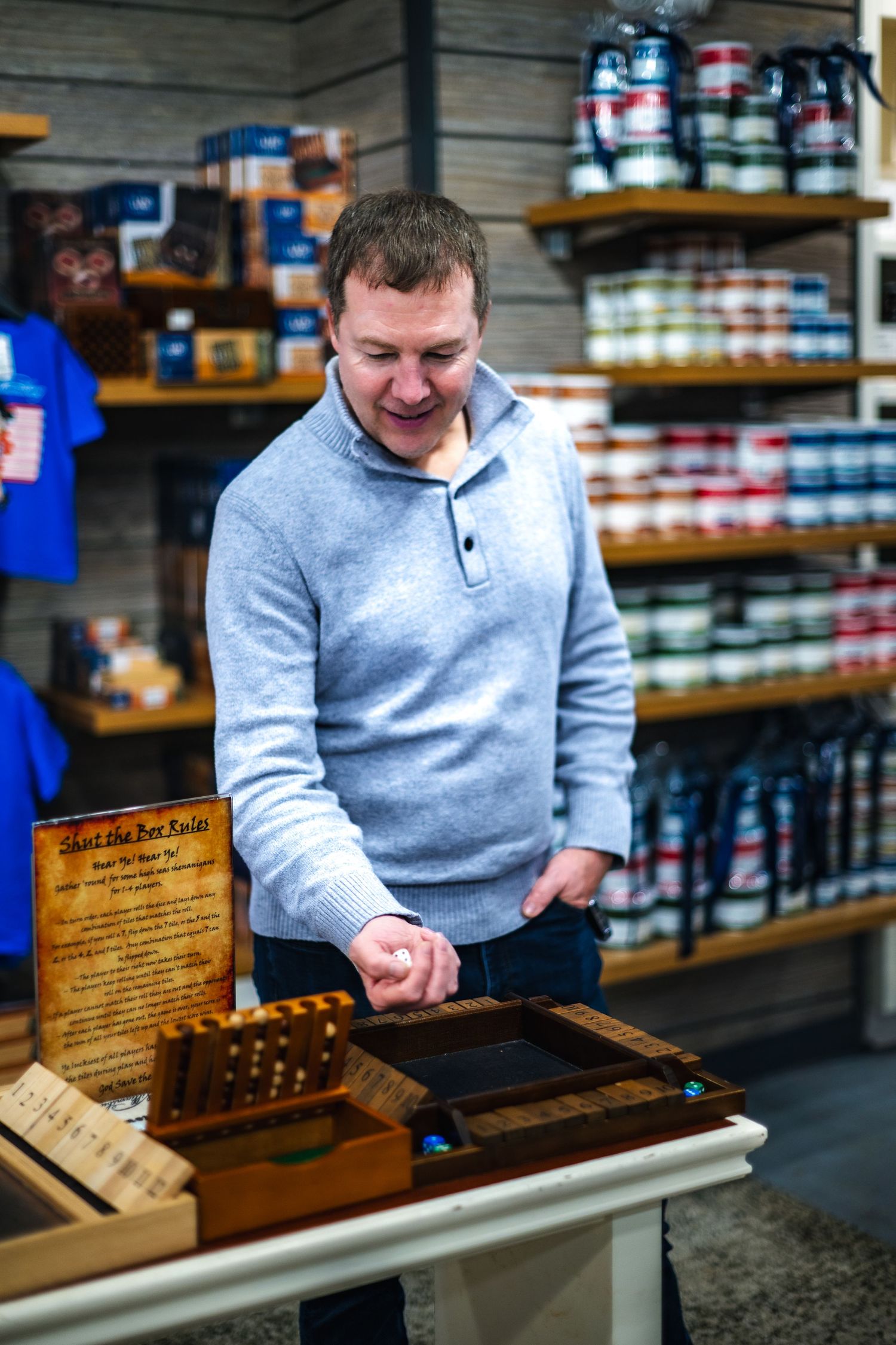 Smiling customer examines wooden display case in retail store with shelves of products in background.