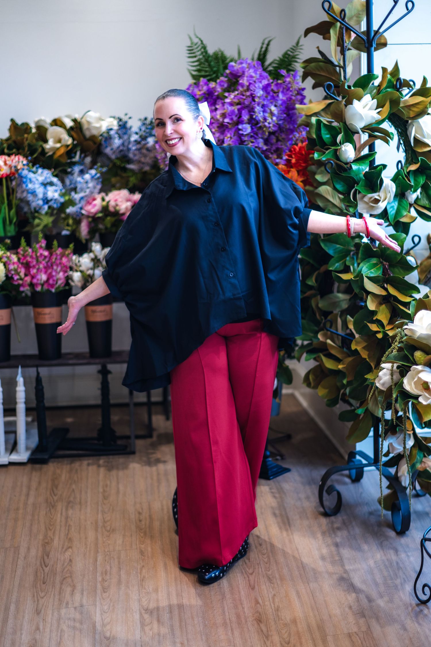 In a floral shop, someone wearing navy oversized top and red wide-leg pants poses among colorful flowers and greenery.