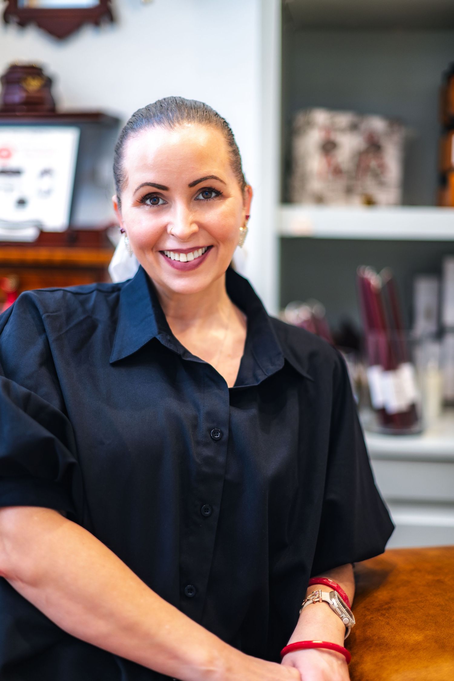 Someone in a black button-down shirt with pulled-back hair stands by a wooden counter in an office setting.