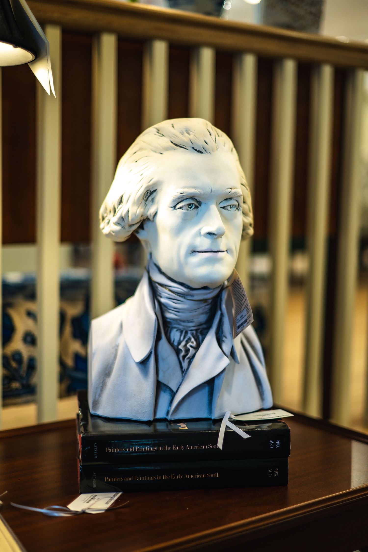 A sculpted grey marble bust of Thomas Jefferson sits atop a dark wooden table with books.