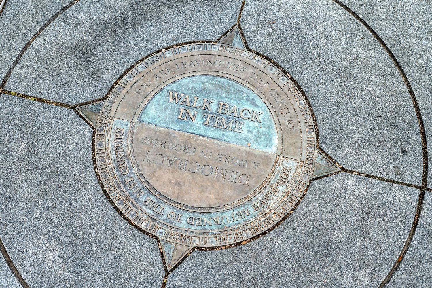 Cracked concrete surrounds a circular metal vault cover with blue and rust colored surface markings.