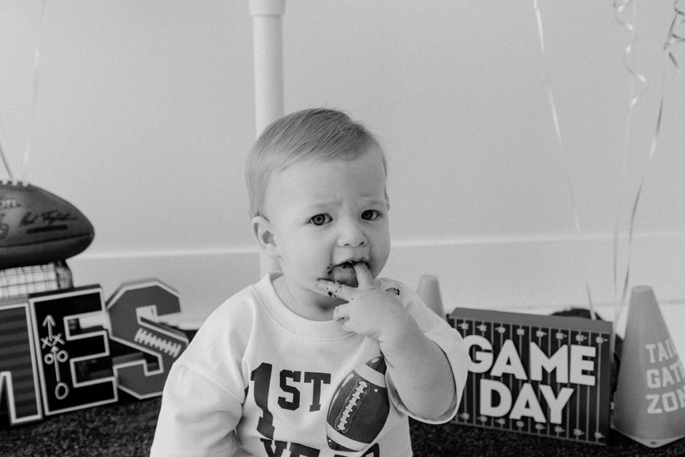 Black and white photo of baby at first birthday party with football themed decorations.
