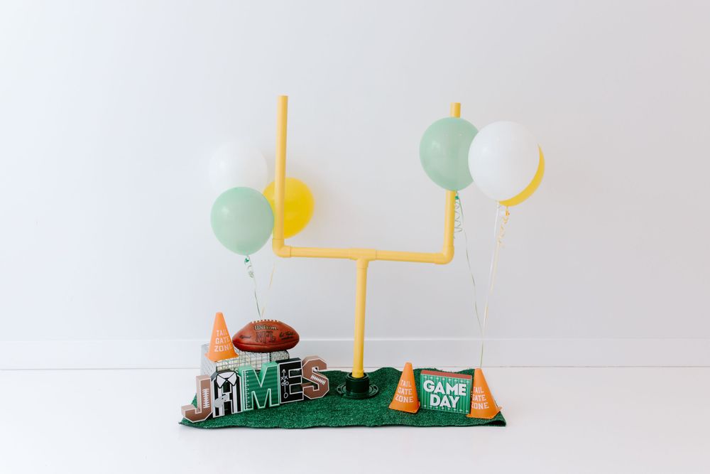 Football themed decor display with yellow goal post, mint green balloons, and turf base with miniature football accessories.