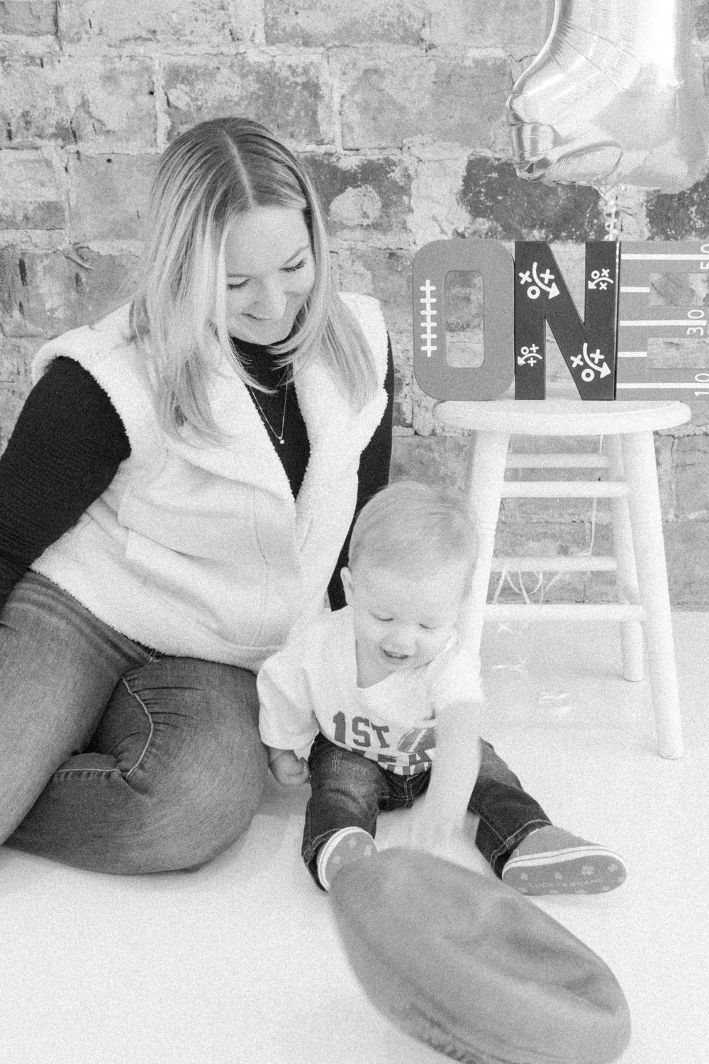 A black and white photo showing a mother and baby sitting together on a floor against a brick wall.