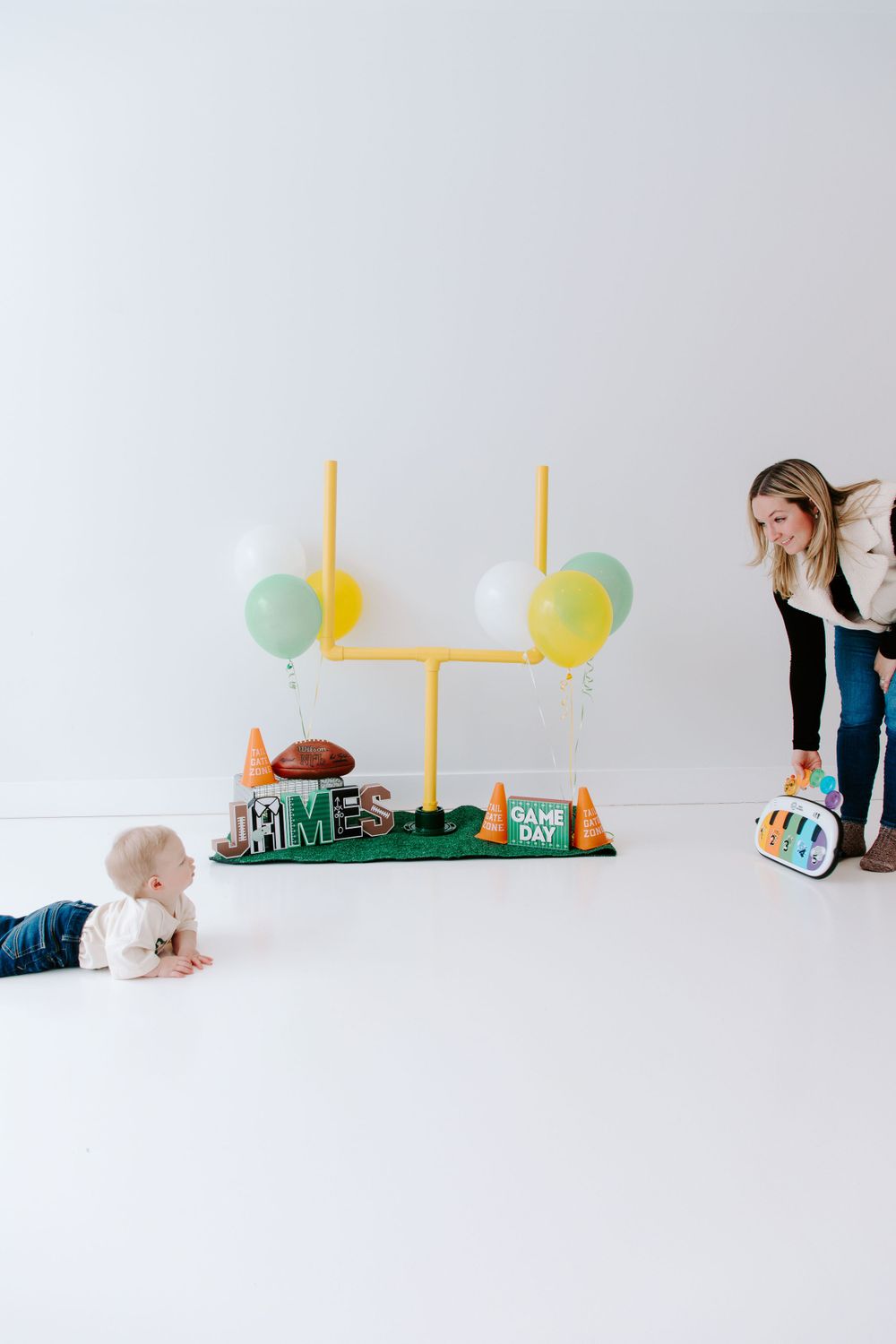 A football-themed party setup with yellow goal posts, green balloons, and field decorations on a white backdrop.