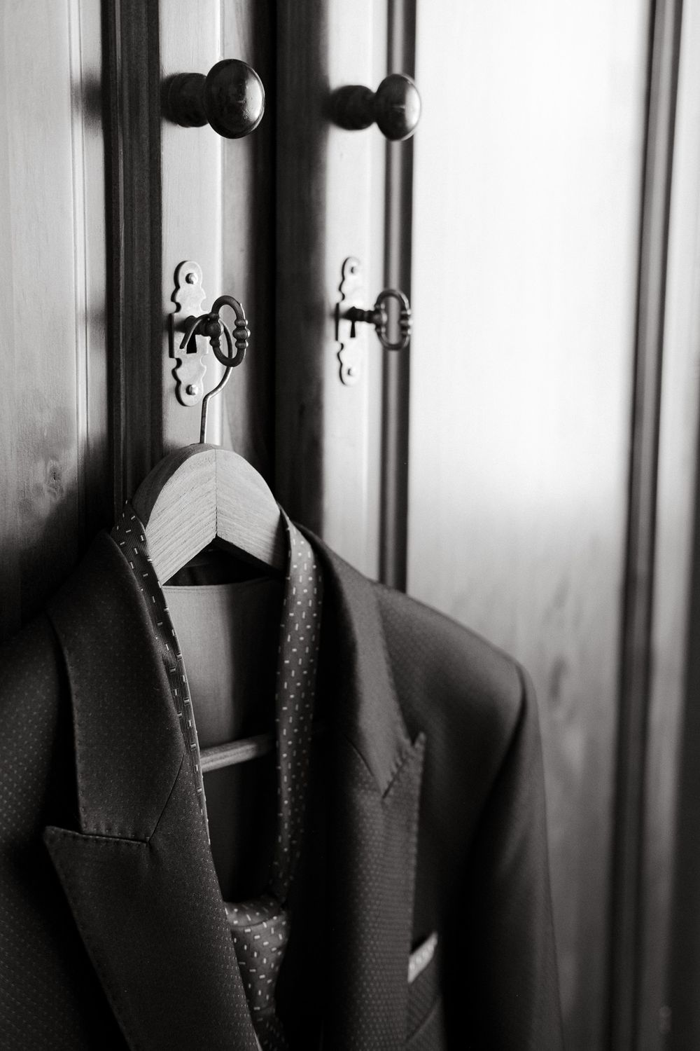 Close-up black and white photo of a suit jacket hanging on an ornate door knob.